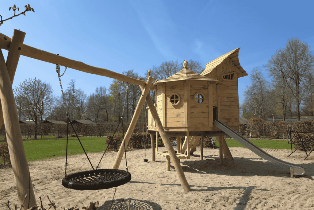 Speeltoestel boomhut op een camping met een uitkijktoren, glijbaan, schommel en zandtafel in het zand
